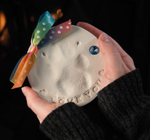 A photo of two hands holding an imprinted Clay Paw with colorful ribbon at the top