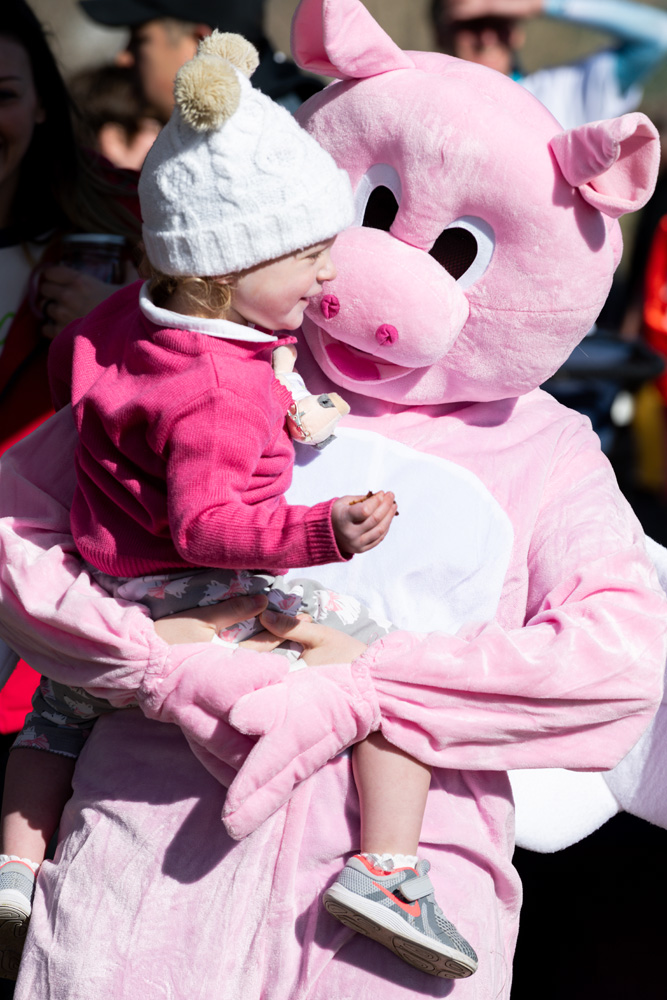 photo of flying pig mascot holding toddler in pink